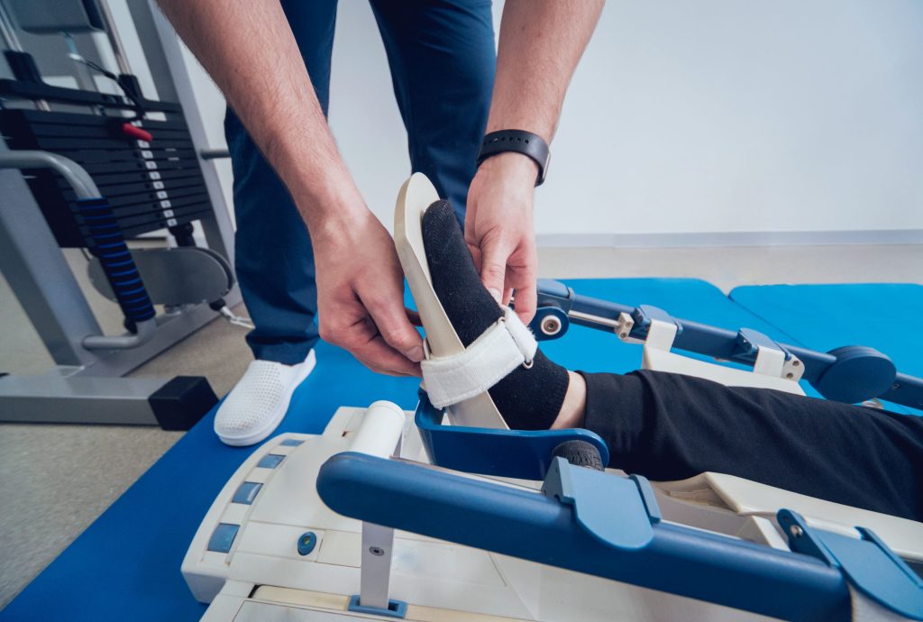 Fizjoterapeuta dostosowujący szynę CPM na nodze pacjenta podczas rehabilitacji po rekonstrukcji mięśni